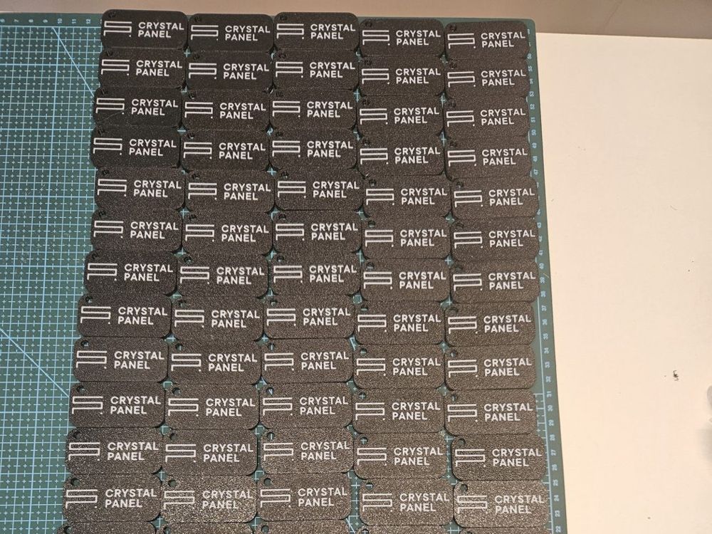 Seria wydrukowanych czarnych breloków z białym logo Crystal Panel ułożonych na macie