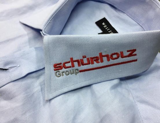 Błękitna koszula z haftowanym logo Schürholz Group na kołnierzyku